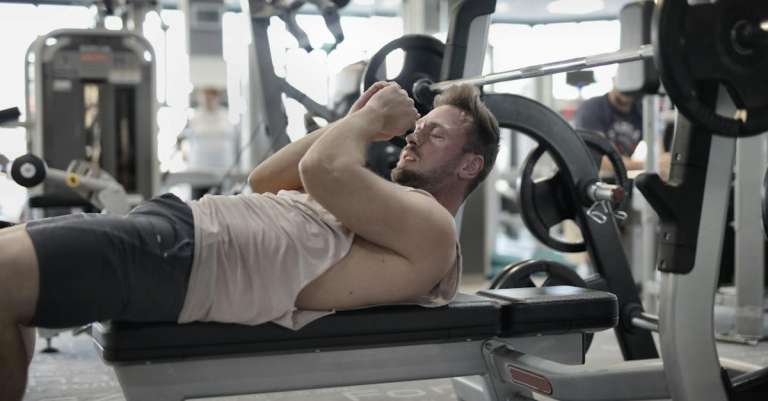 geconcentreerde-gespierde-sportman-bankdrukken-in-de-sportschool-voorbereiden