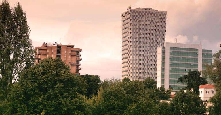 hoge-gebouwen-in-de-buurt-van-groene-blad-bomen-onder-witte-hemel-overdag