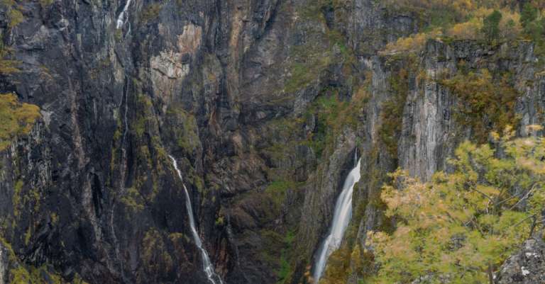 Waterval in bergachtig landschap met herfstbomen.