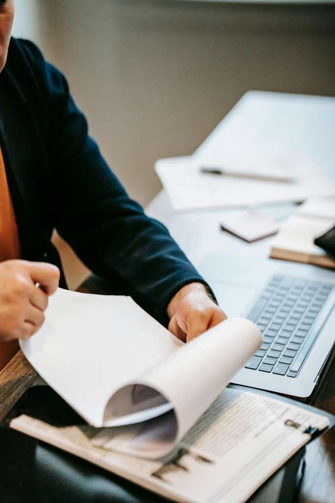 Zakelijke professional leest document naast laptop.